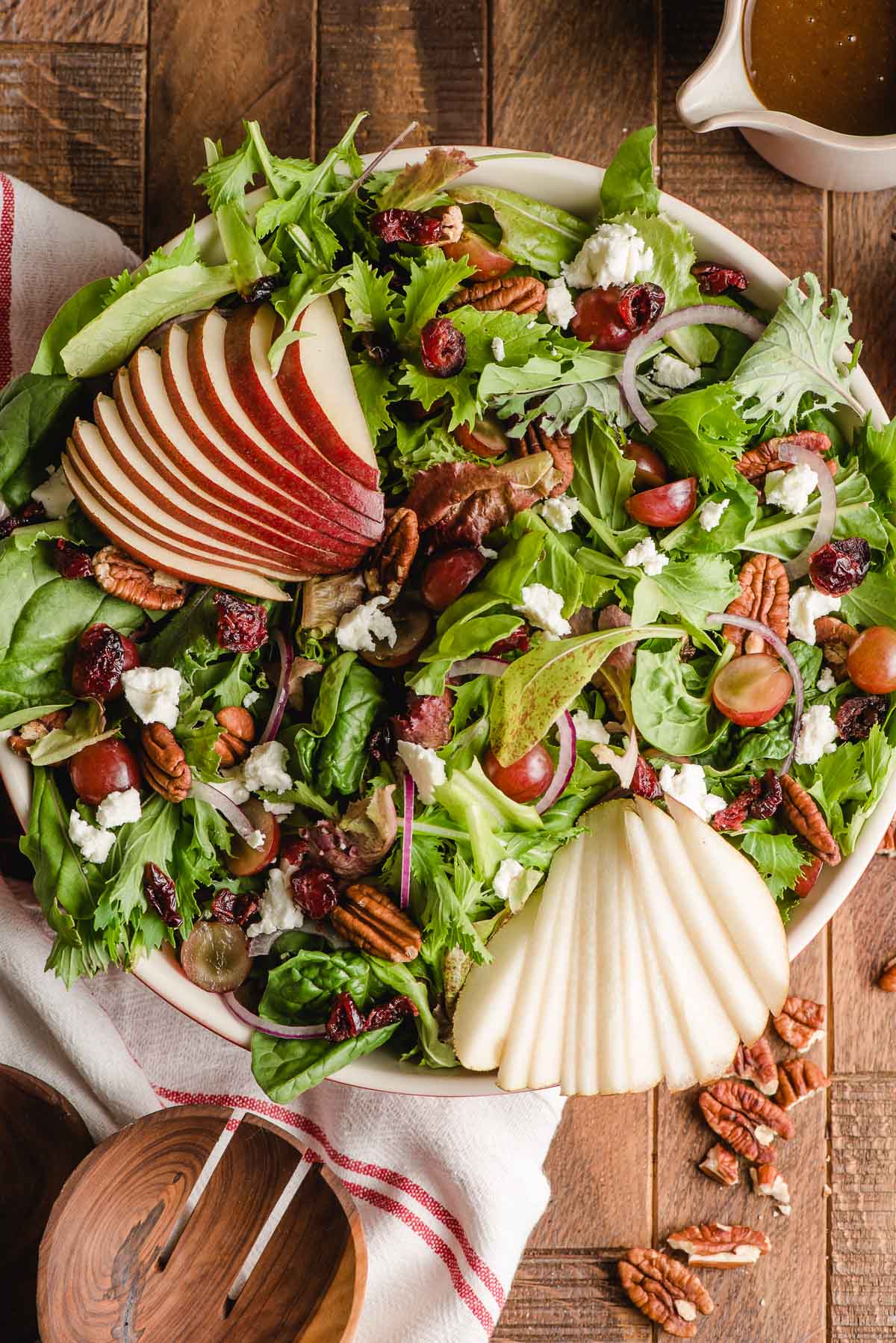 Large bowl with a mixed green salad, sliced pears, cranberries, and goat cheese.