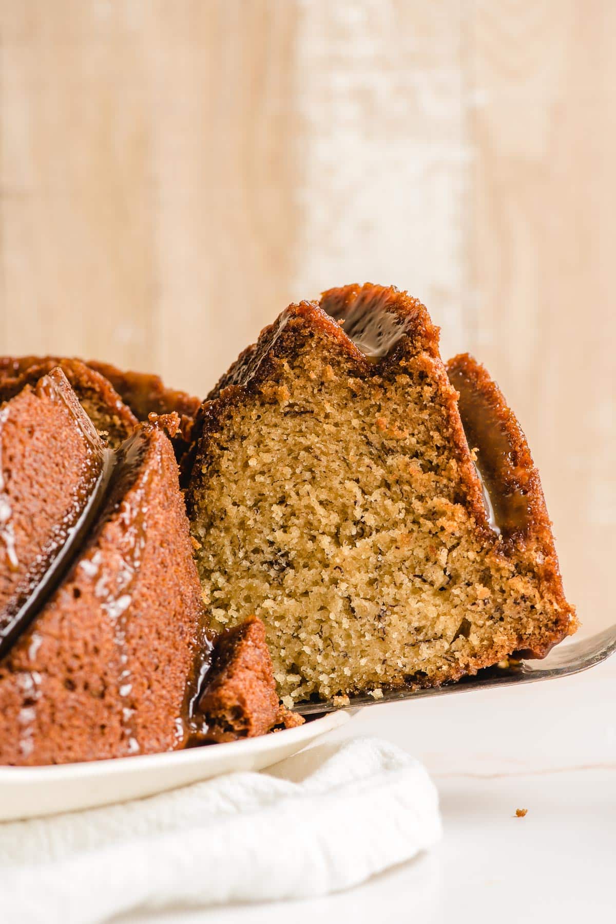 A slice of Banana Caramel Cake being lifted off a serving platter.