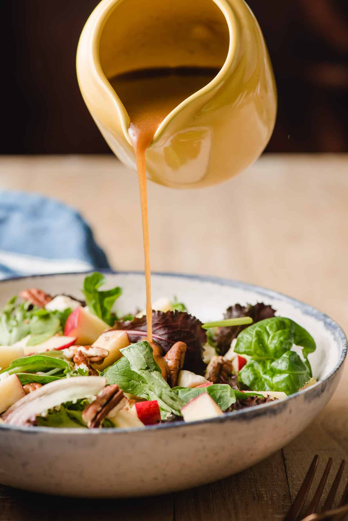 Maple dressing being drizzled on a salad with apples and feta.