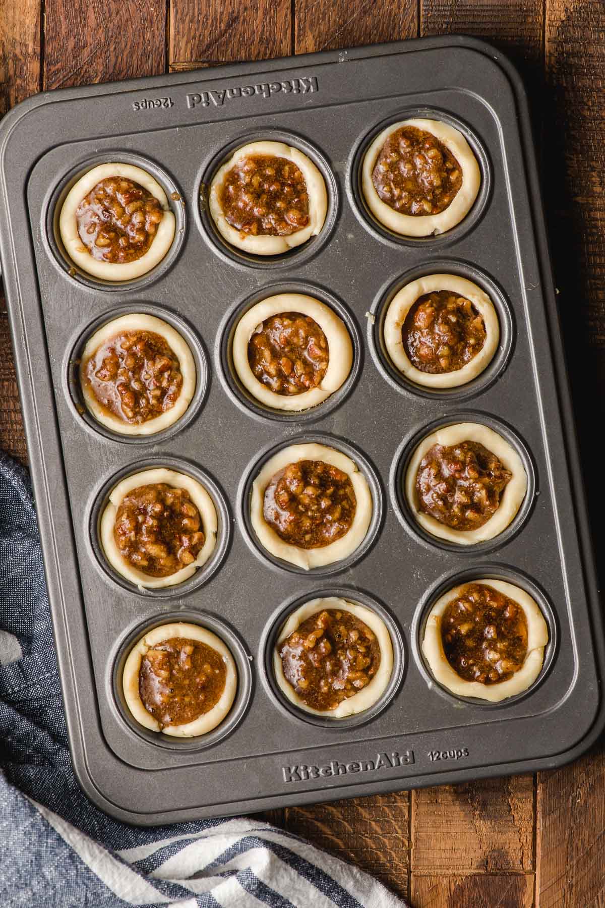Mini muffin tray filled with unbaked pecan tassies.