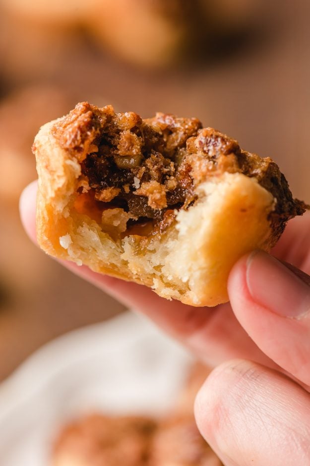 Hand holding a pecan tassie with a bite taken out of it.