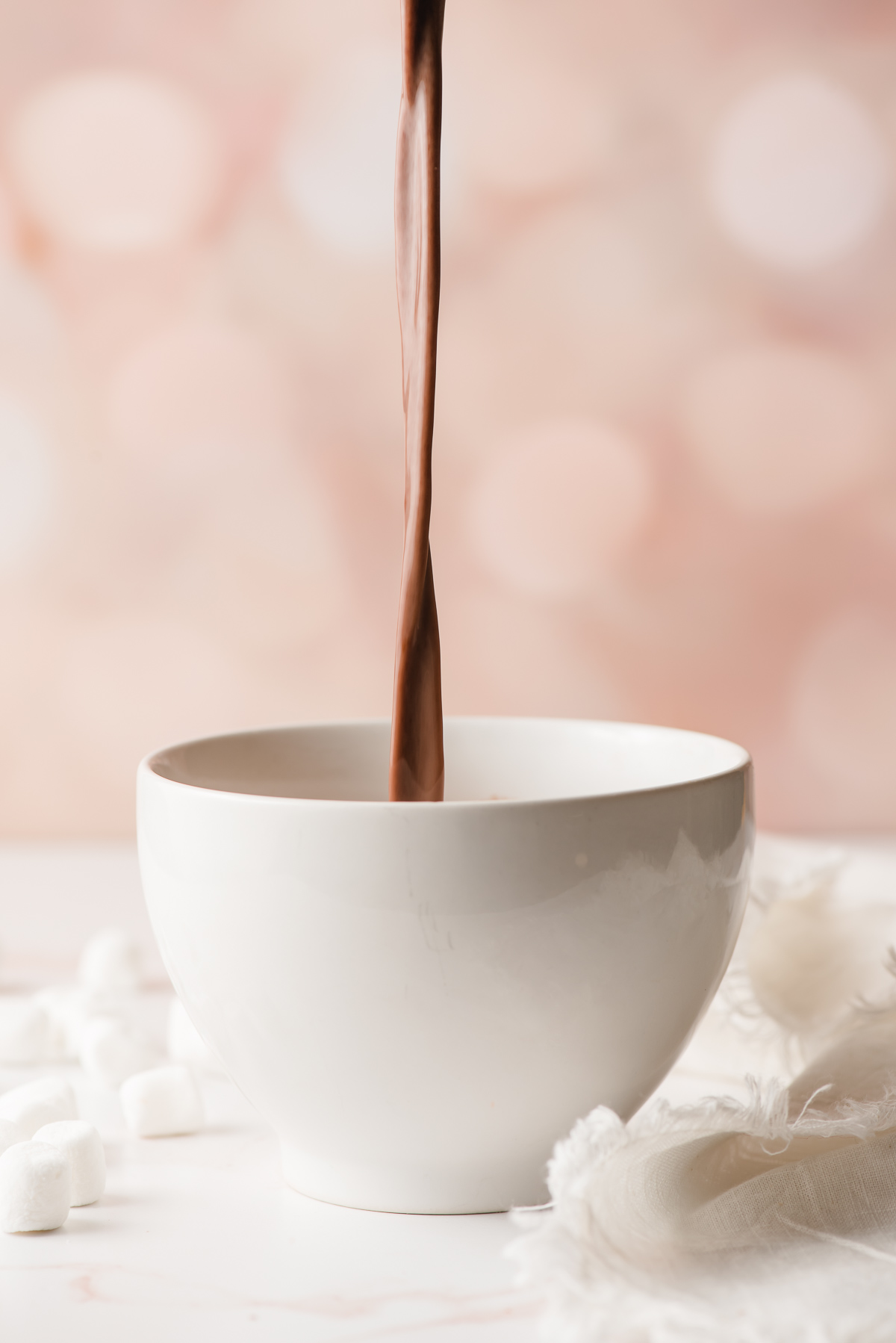 Hot chocolate being poured from a sauce pot into a white mug.