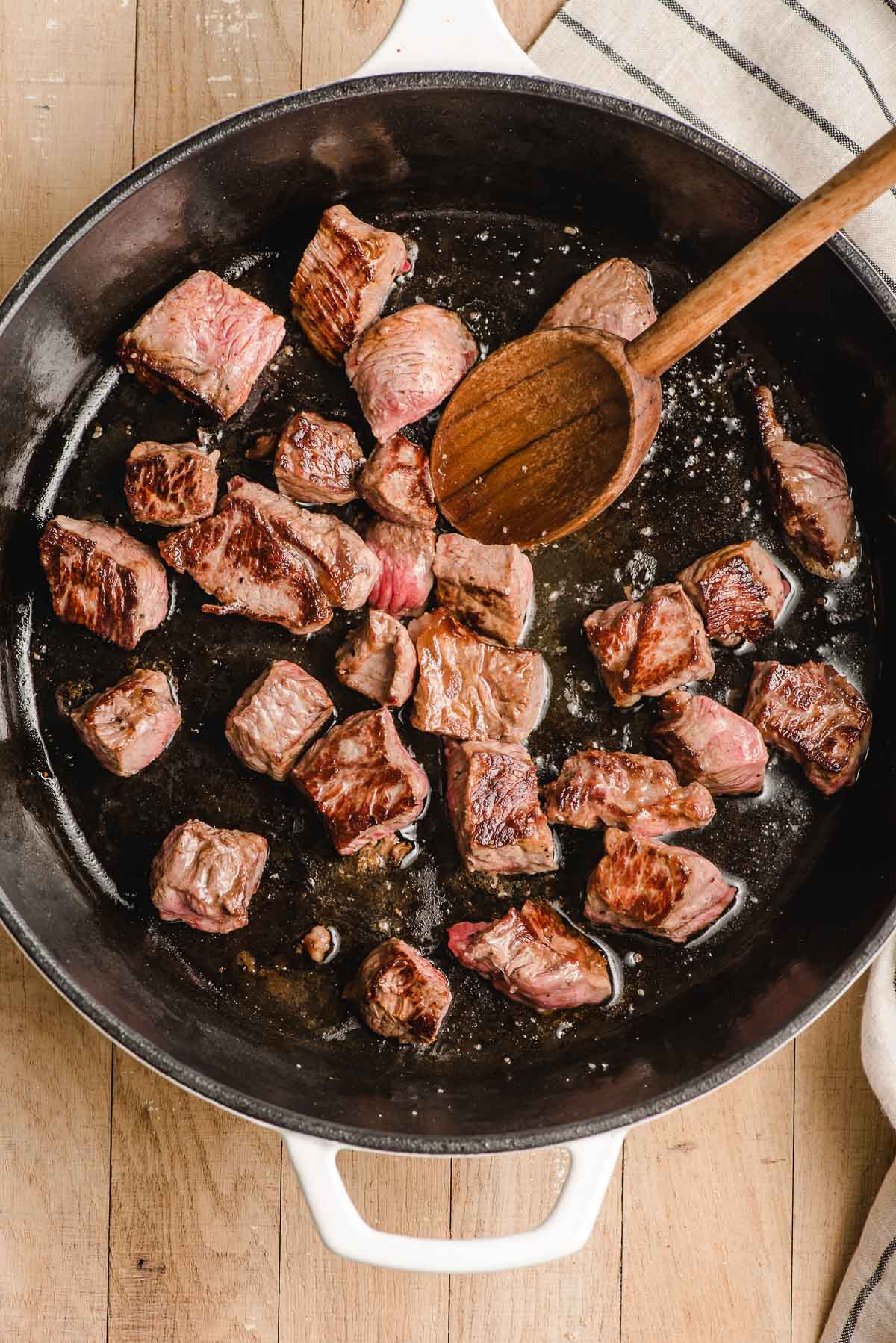 Steak bites being seared in a cast iron skillet.