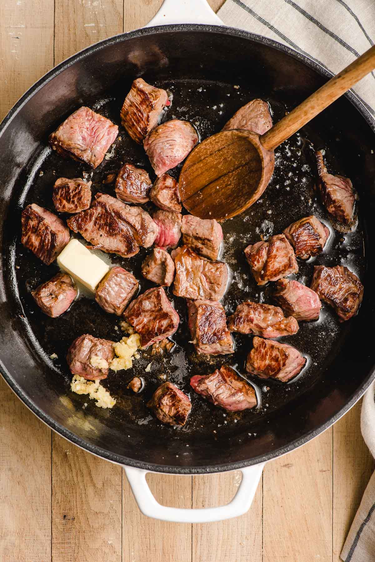 Hibachi steak bites shown cooking in a skillet with a pat of butter and minced garlic.