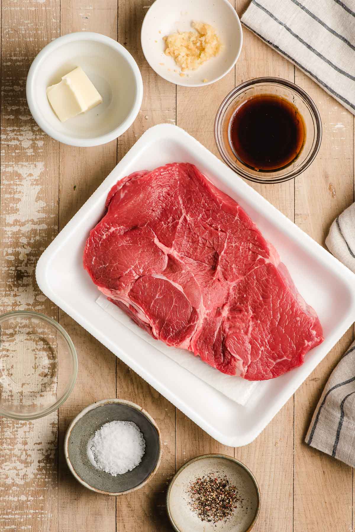 Ingredients for a hibachi steak recipe on a wood background--sirloin steak, salt, pepper, oil, garlic, butter, soy sauce, mirin, sugar.