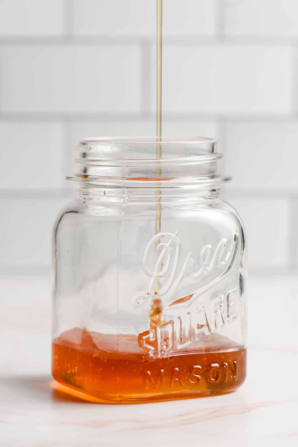Honey being poured into a glass mason jar.