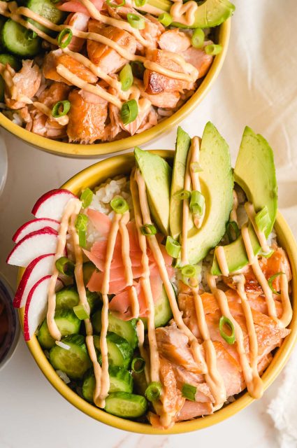 Salmon sushi bowl with cucumber, avocado, radish, pickled ginger, and spicy mayo drizzled on top.