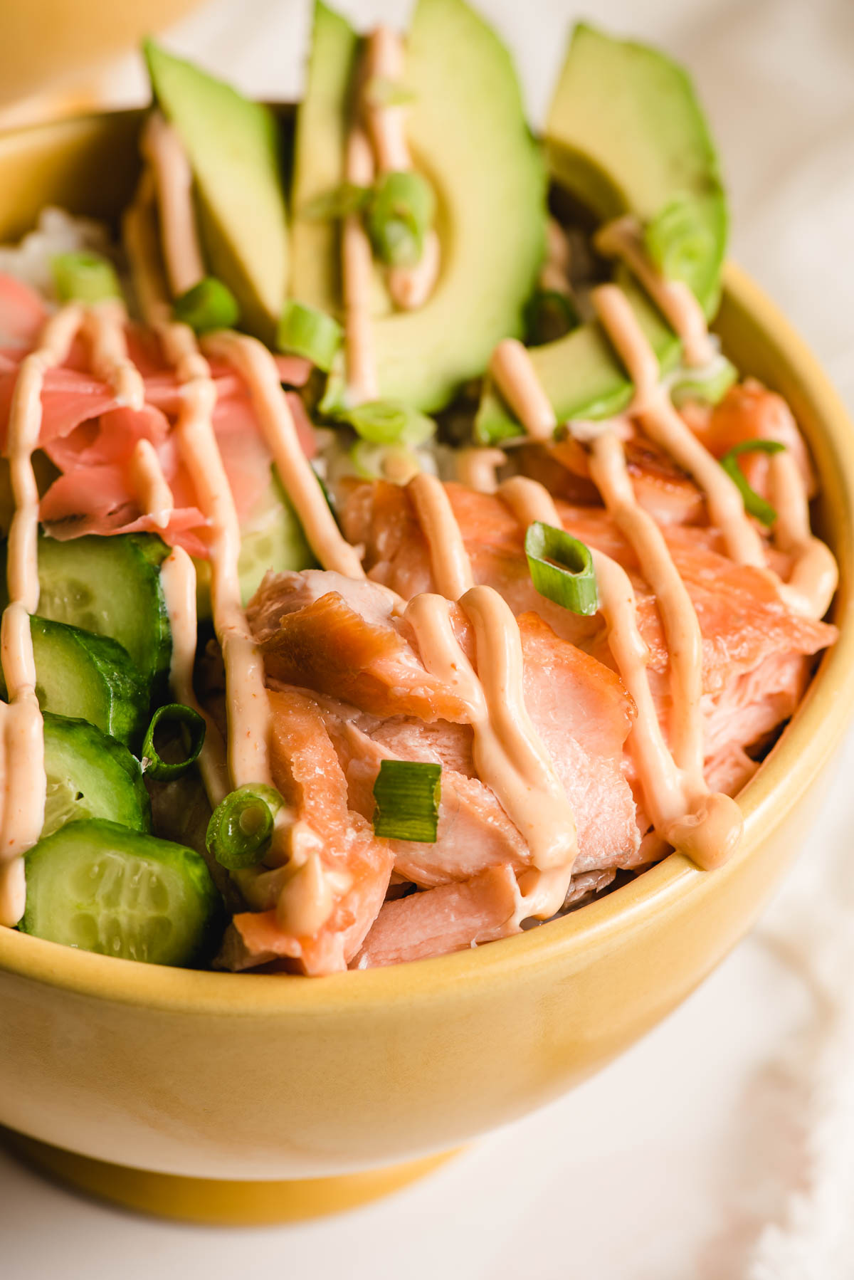 Spicy mayonnaise drizzled over broiled salmon, sliced cucumber and avocado, and sushi rice.