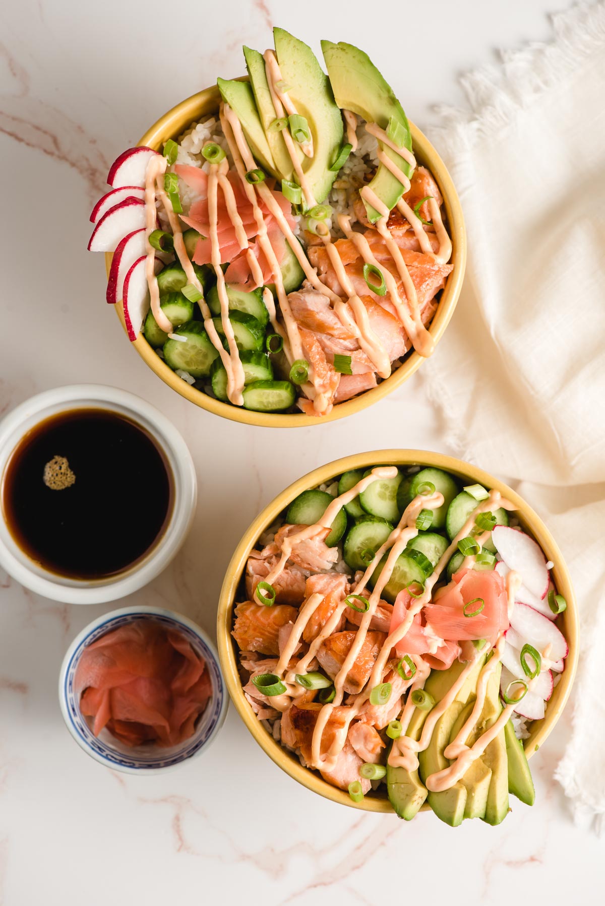 Two Salmon Sushi Bowls with cups of eel sauce and pickled ginger on the side.