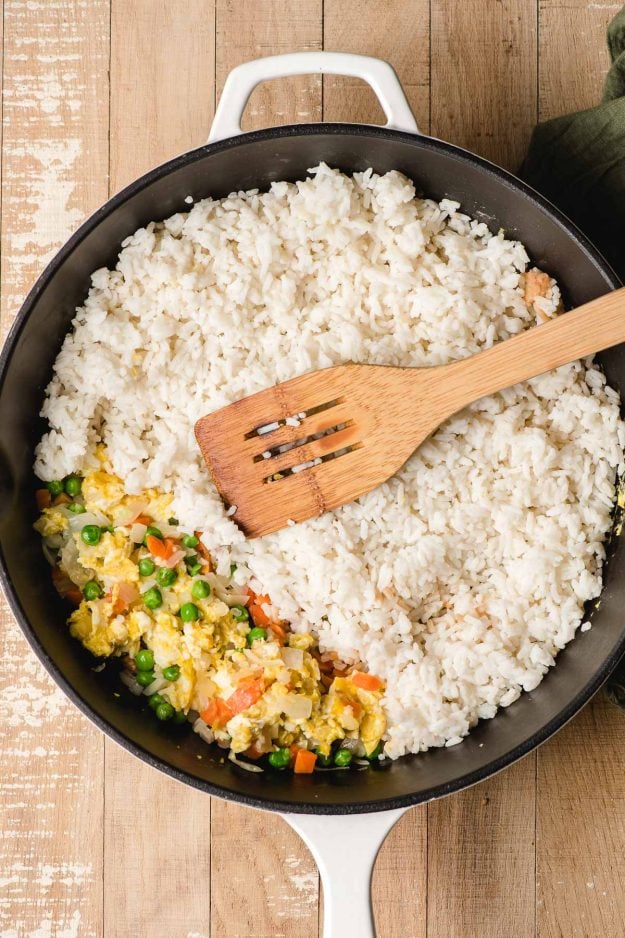 Cooked white rice added to a skillet with peas, carrots, and egg.