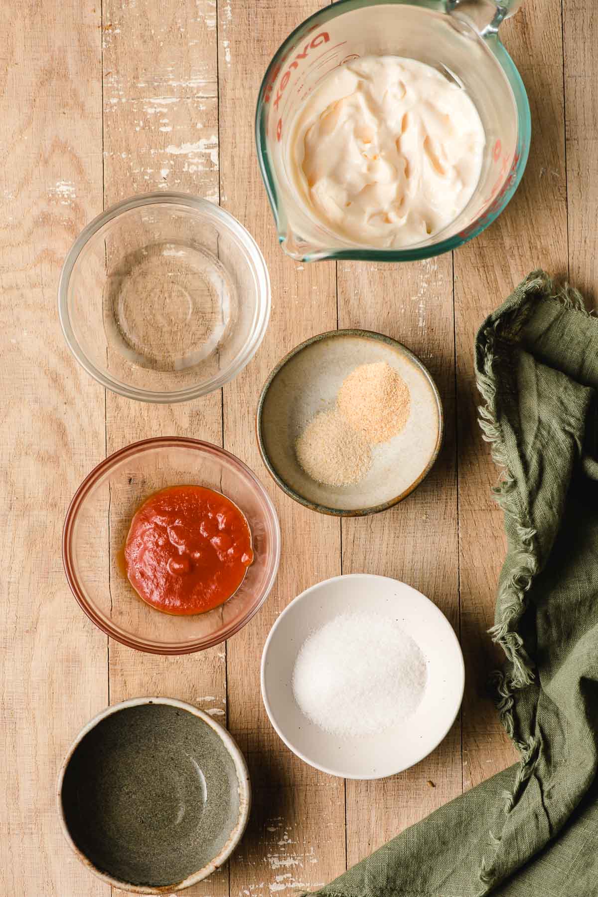 Multiple prep bowls holding mayonnaise, mirin, sriracha, vinegar, garlic powder, and onion powder.