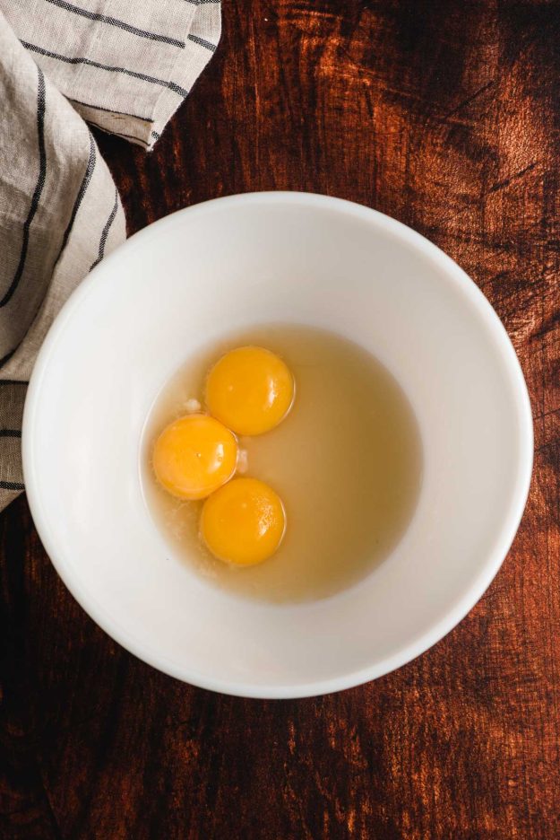Three egg yolks, sugar, and rum in a white bowl.