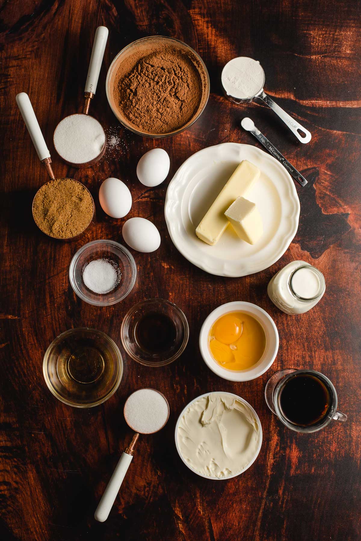 Ingredients for brownies on a wood background, including eggs, sugar, butter, flour, salt, and cocoa powder.