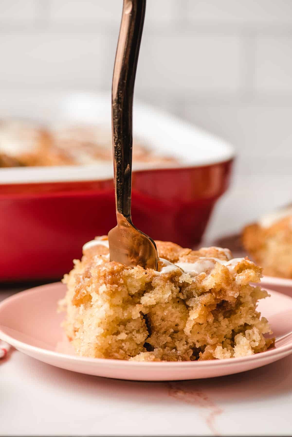 A slice of Banana Crumble Cake on a plate with a fork sticking in it.