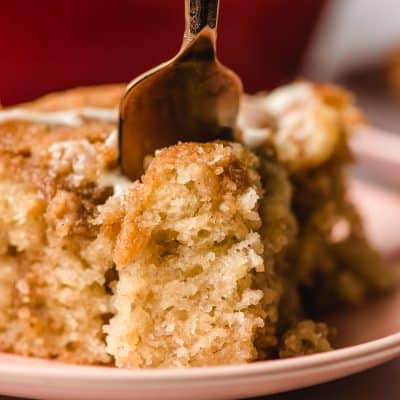 Golden fork stabbing a piece of banana crumb cake on a plate.