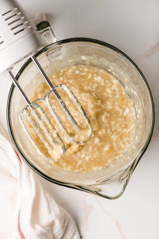 Butter and bananas beaten together in a glass mixing bowl.