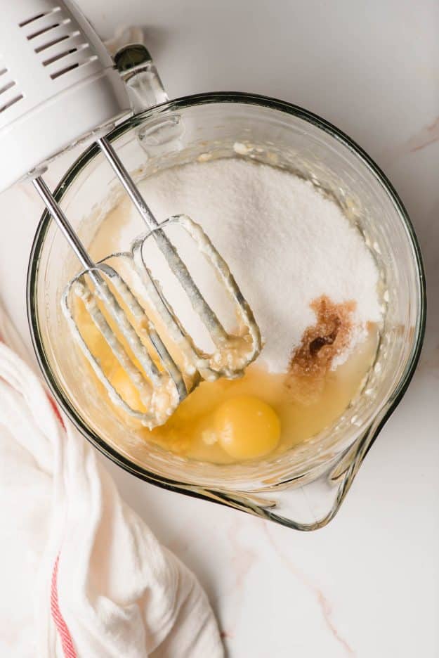 Electric beater beating eggs, sugar, and vanilla into butter and bananas.