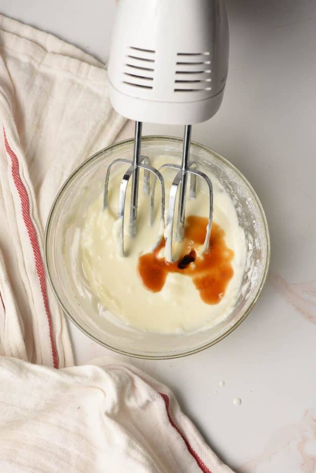 Electric beater whisking together cream cheese, powdered sugar, and vanilla.