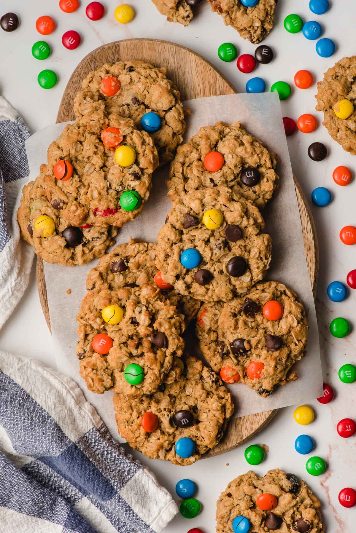 A stack of Gluten Free Monster Cookies on a serving board surrounded by M&Ms and a napkin.