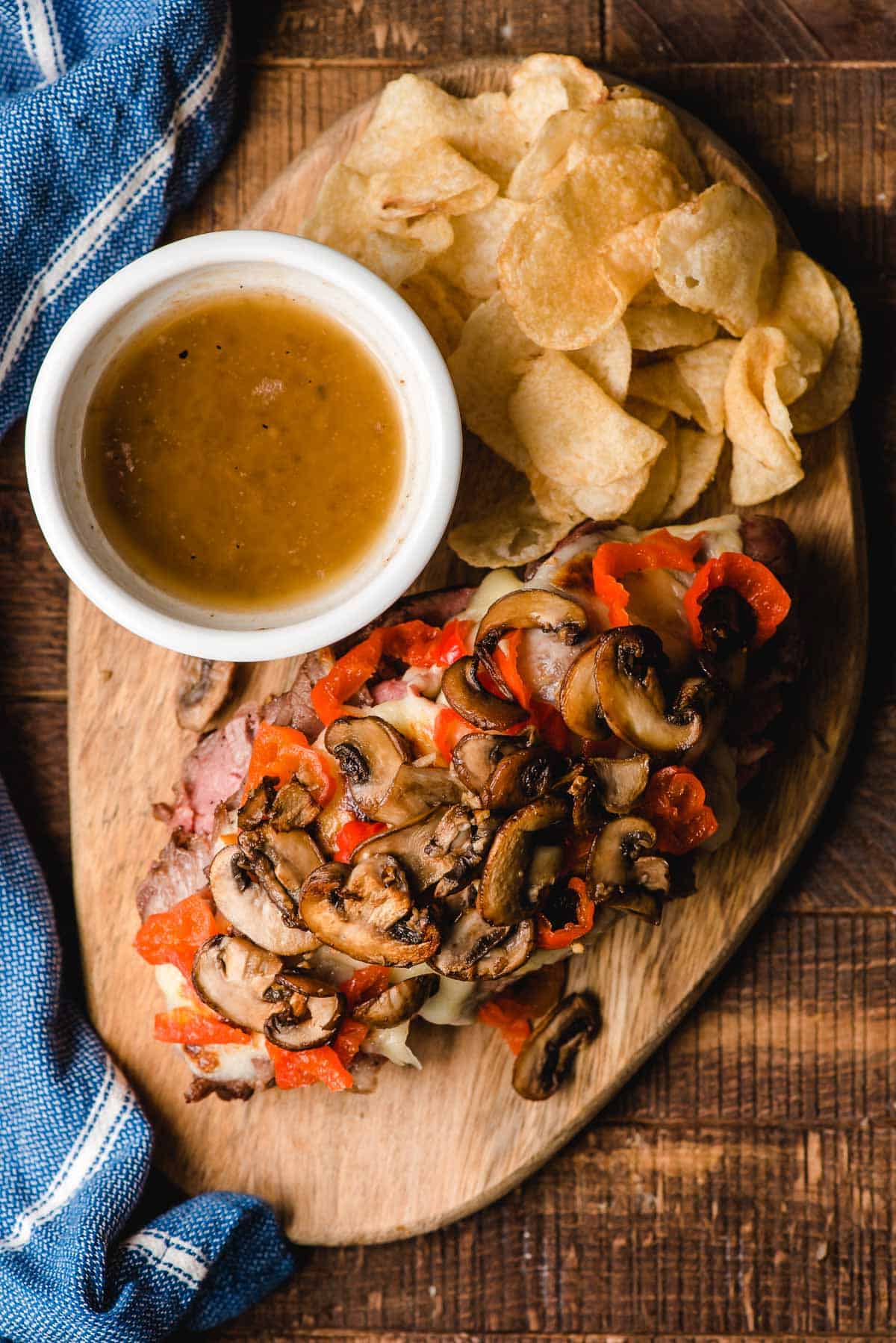 French dip prime rib sandwich on a cutting board with au jus and chips.