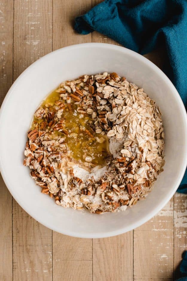 White bowl with oats, flour, pecans, salt, and melted butter.