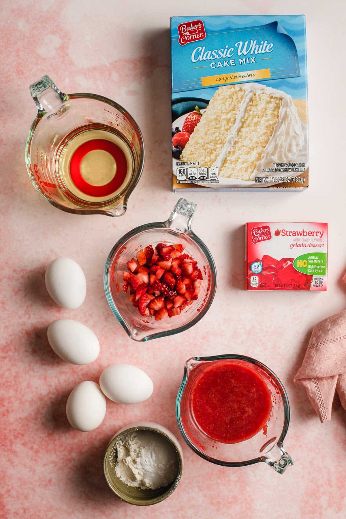 White cake mix, oil, eggs, chopped strawberries, pureed strawberries, and strawberry jello on a pink background.