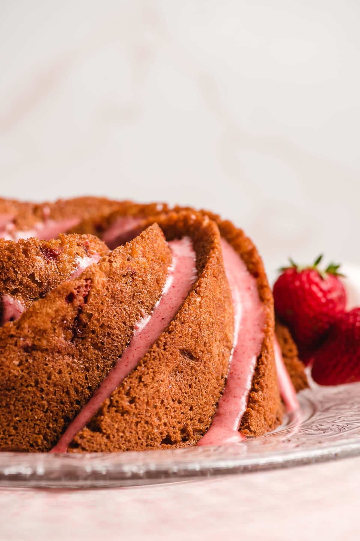 Strawberry Bundt Confection on a glass serving dish with fresh strawberries in the background.