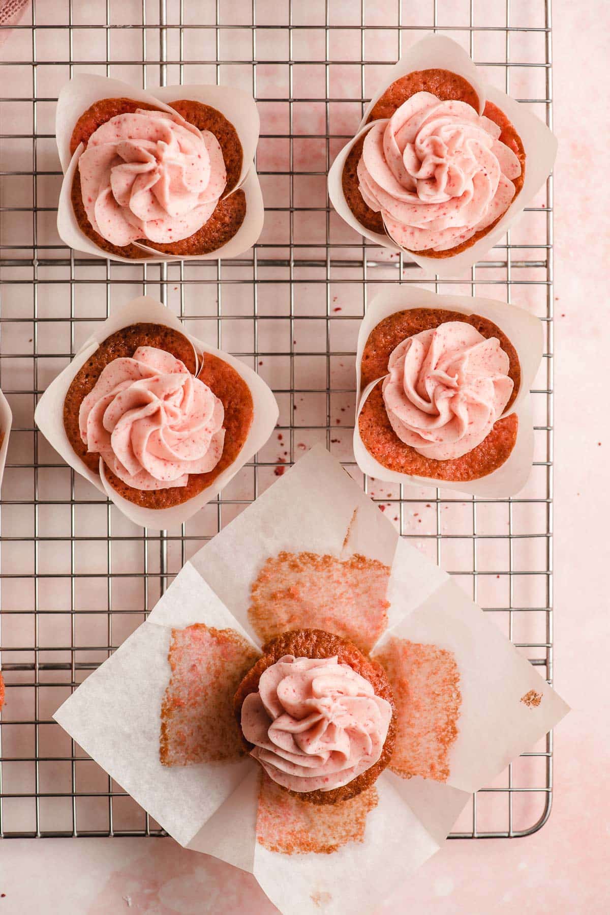 Strawberry cupcakes in parchment paper lines on a cooling rack.