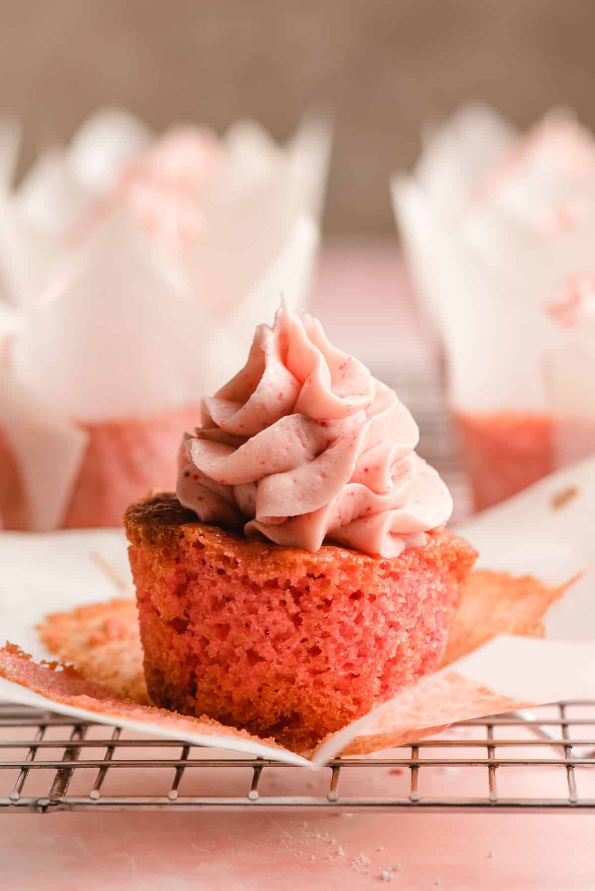 Strawberry cupcake with a parchment paper liner peeled off around it.