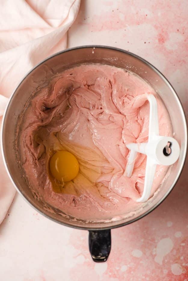 Strawberry cake batter with an egg in a mixing bowl.