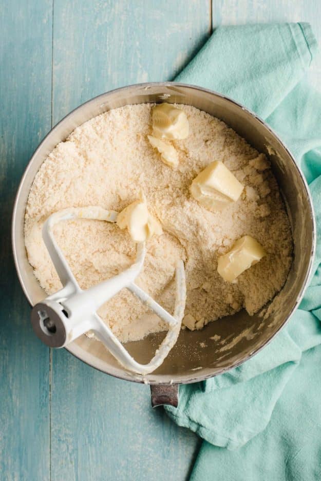 Bowl of an electric mixer with dry ingredients and chunks of butter being incorporated into it.