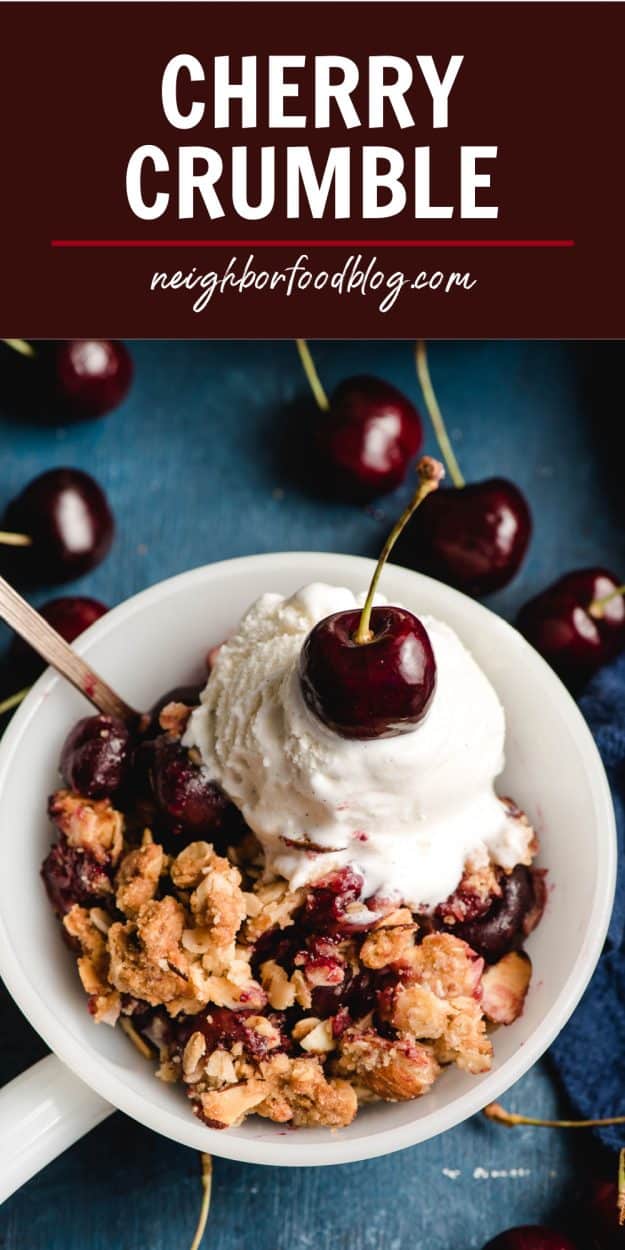 Scoop of cherry crumble topped with ice cream and a cherry, in a white bowl.