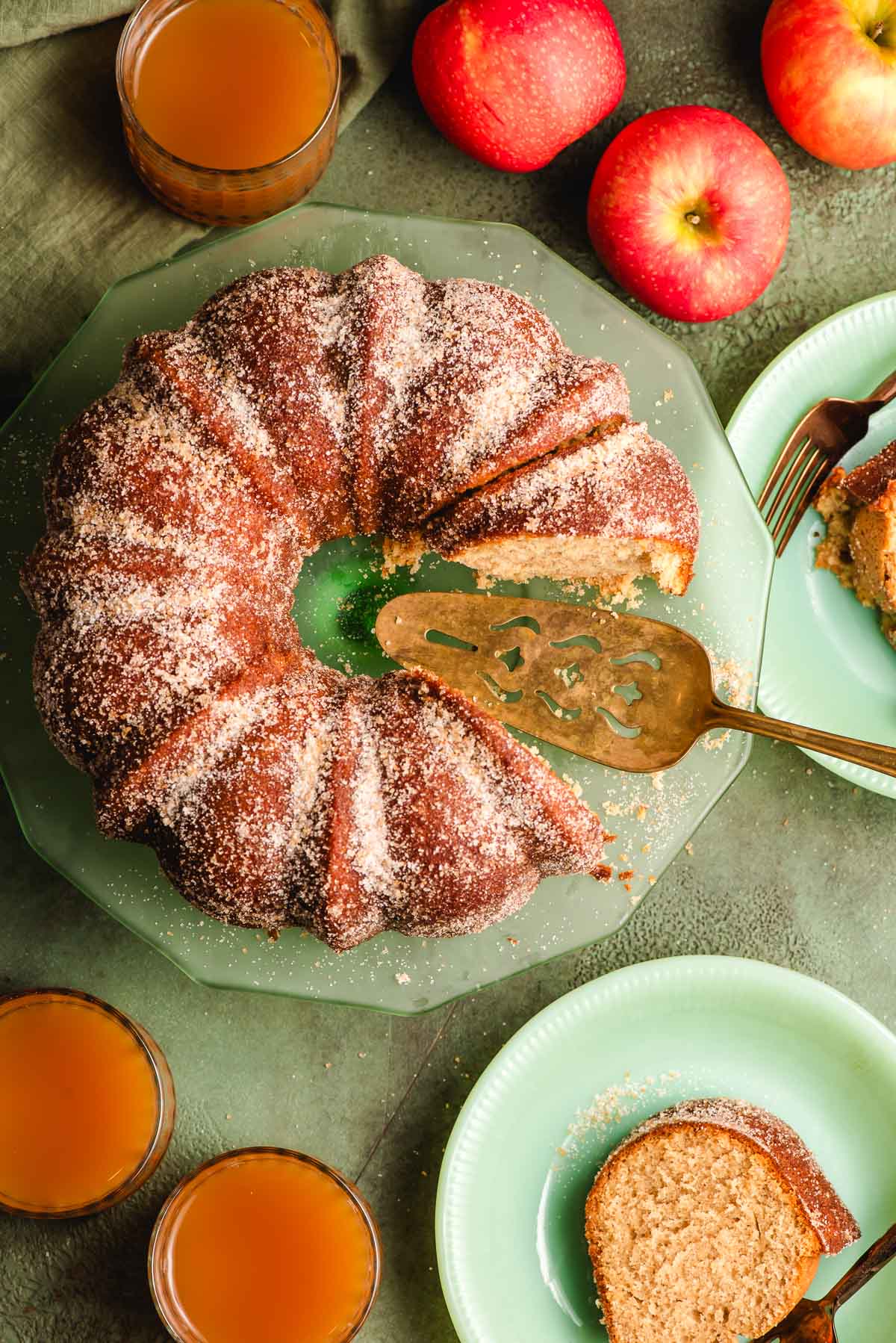 Cinnamon sugar coated apple cider donut cake with a few sliced taken out of it and a vintage gold pie server.