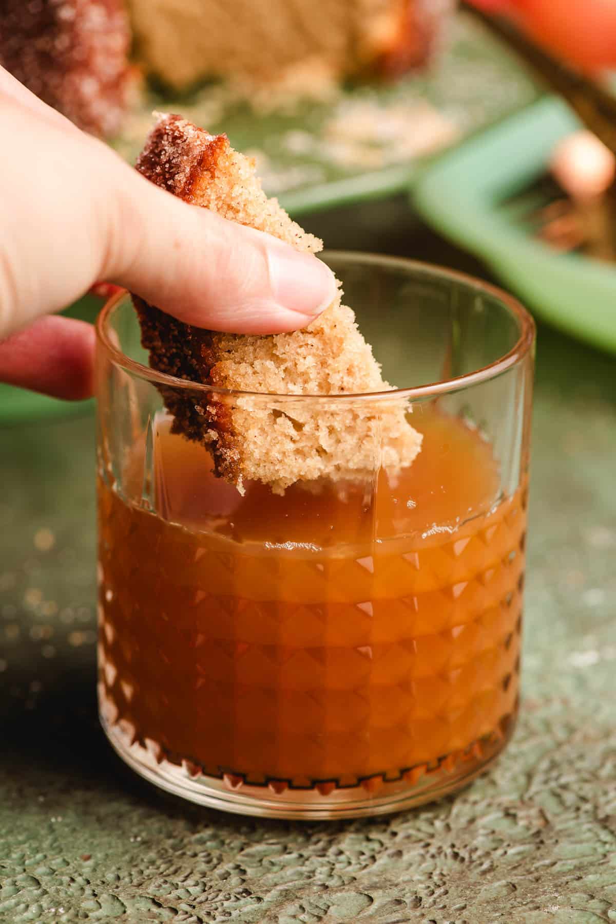 Slice of cider cake being dunked into a glass of apple cider.