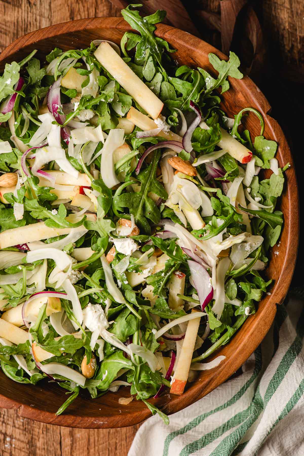 Arugula, fennel, and world salad with goat cheese and almonds in a wooden bowl.