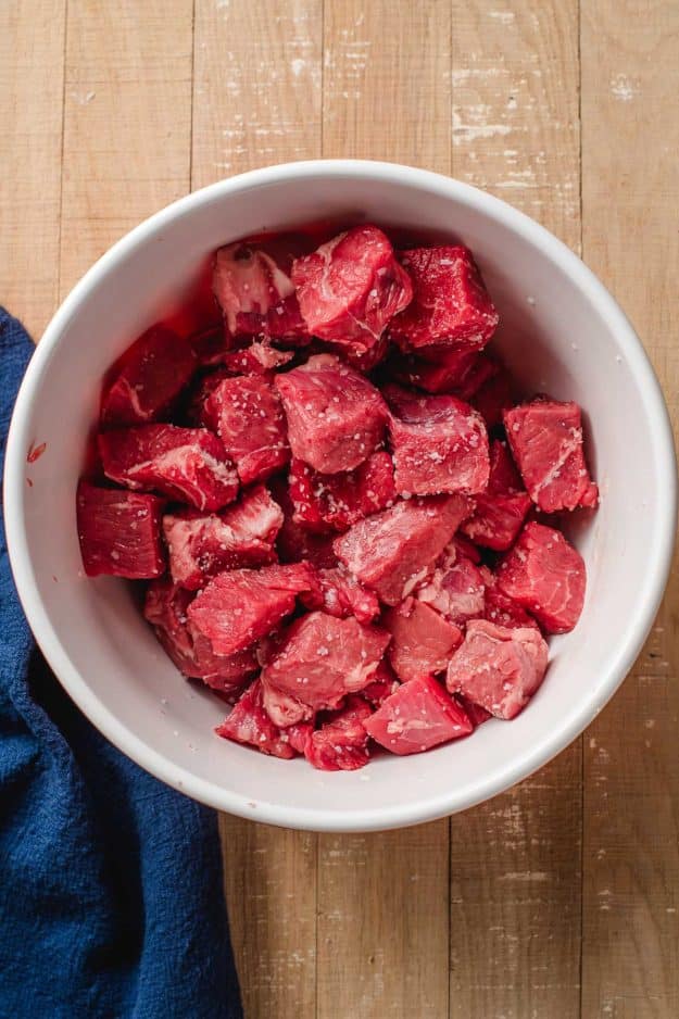Sirloin steak cut into cubes and tossed with salt in a bowl.