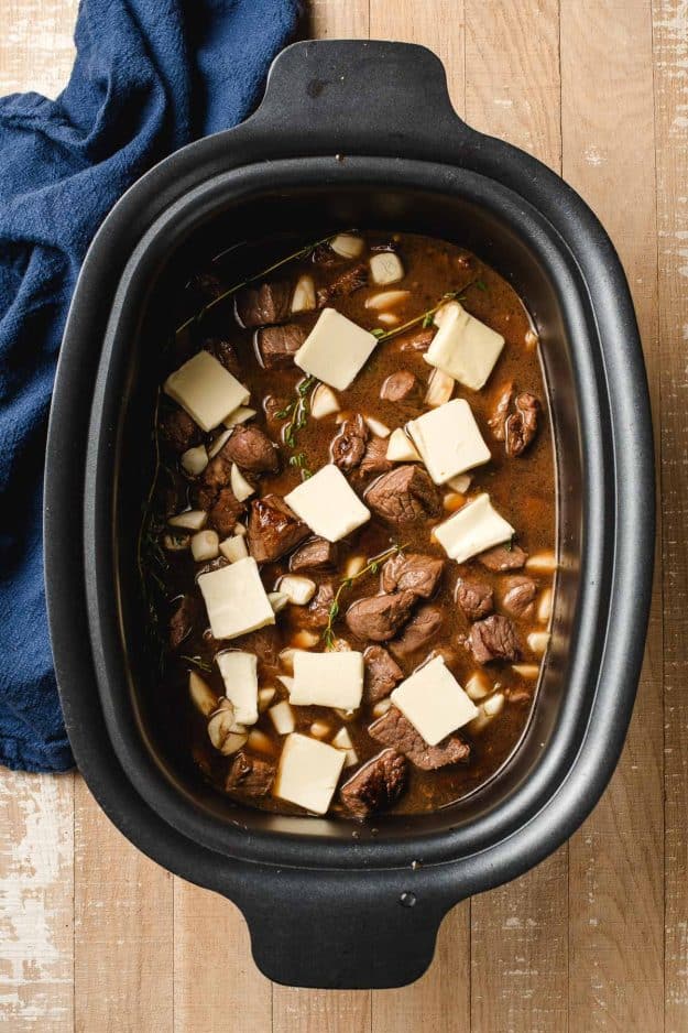 Seared steak bites, whinge broth, thyme, garlic cloves, and slices of butter in a slow cooker.