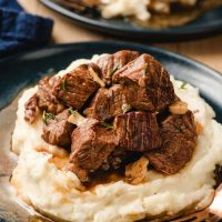 Blue plate stacked with mashed potatoes and slow cooker steak bites.