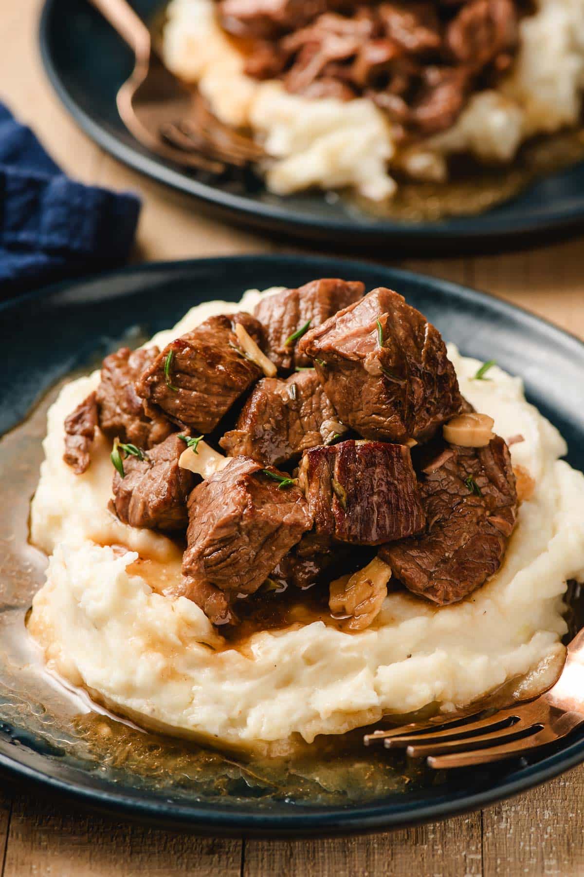 Blue plate stacked with mashed potatoes and slow cooker steak bites.