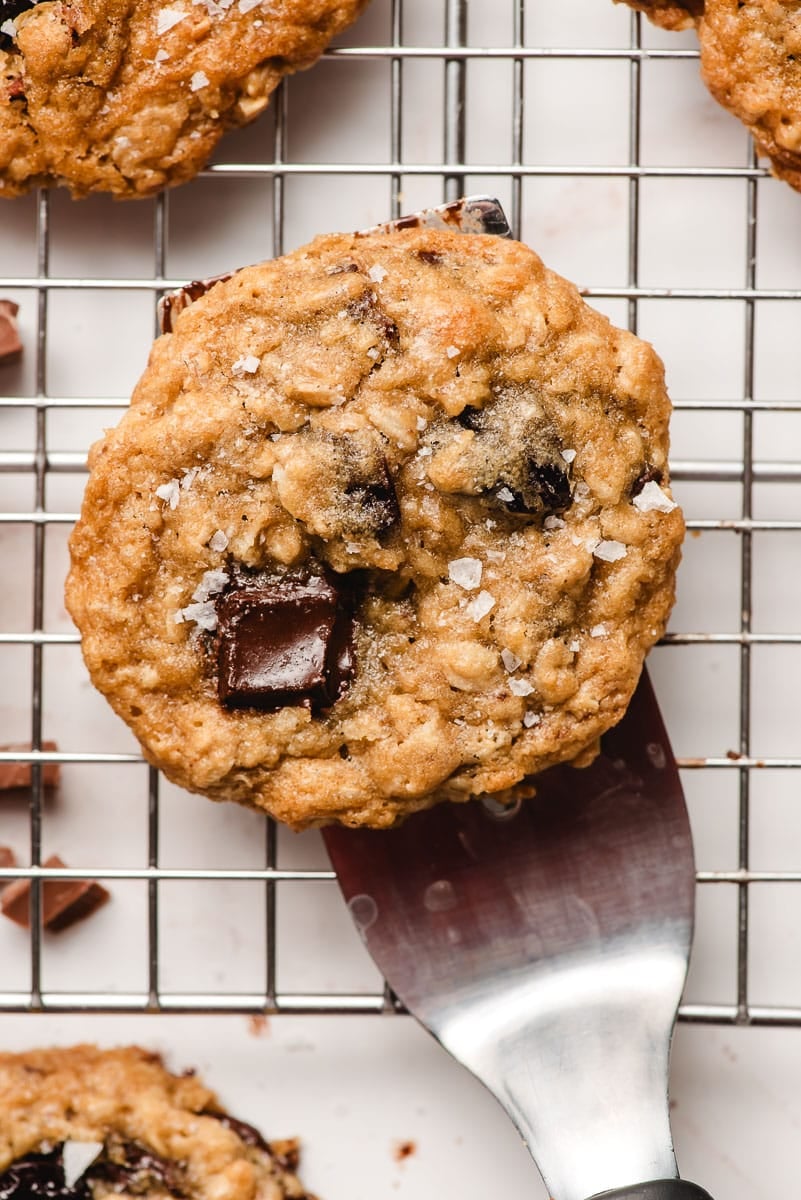 A spatula places a freshly baked cherry oatmeal cookie on a cooling rack.