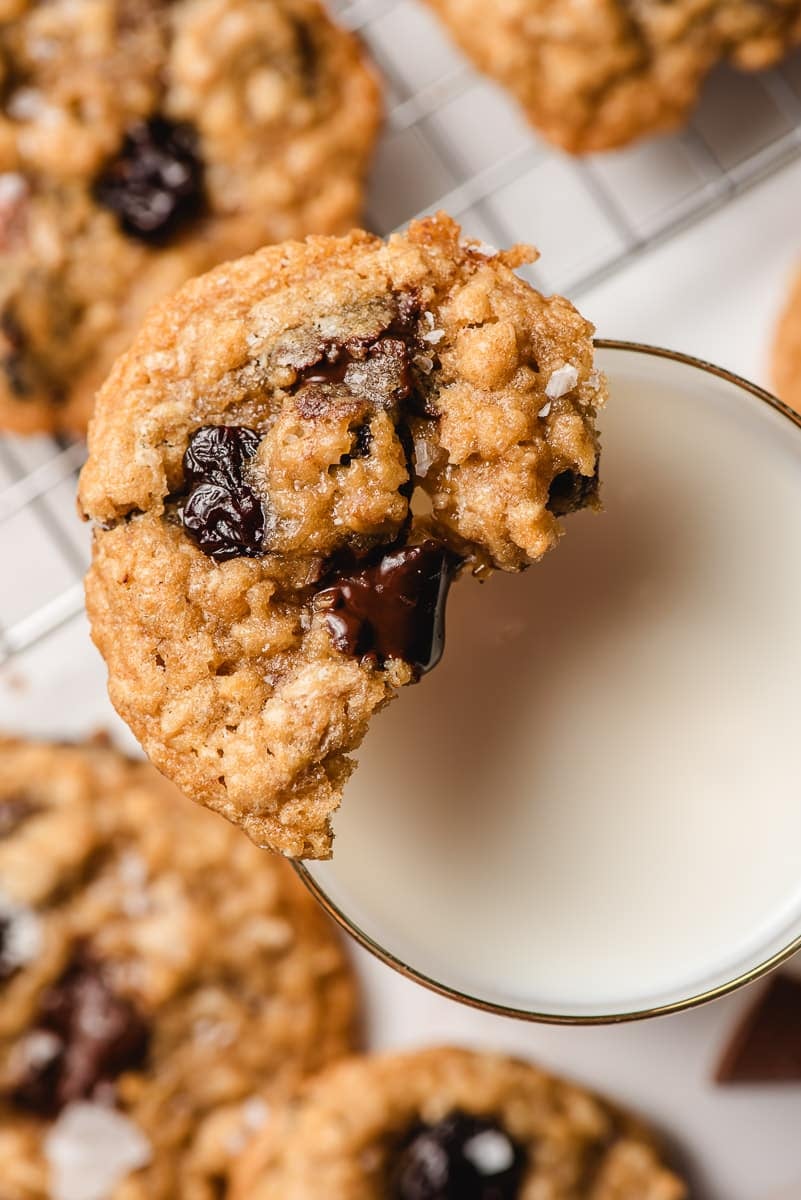 Half a cookie on a glass of milk with cookies in the background.