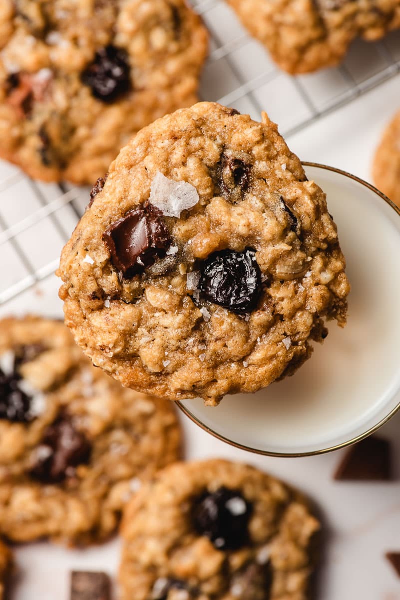 A chocolate chip cherry oatmeal cookie balances on top of a glass of milk.