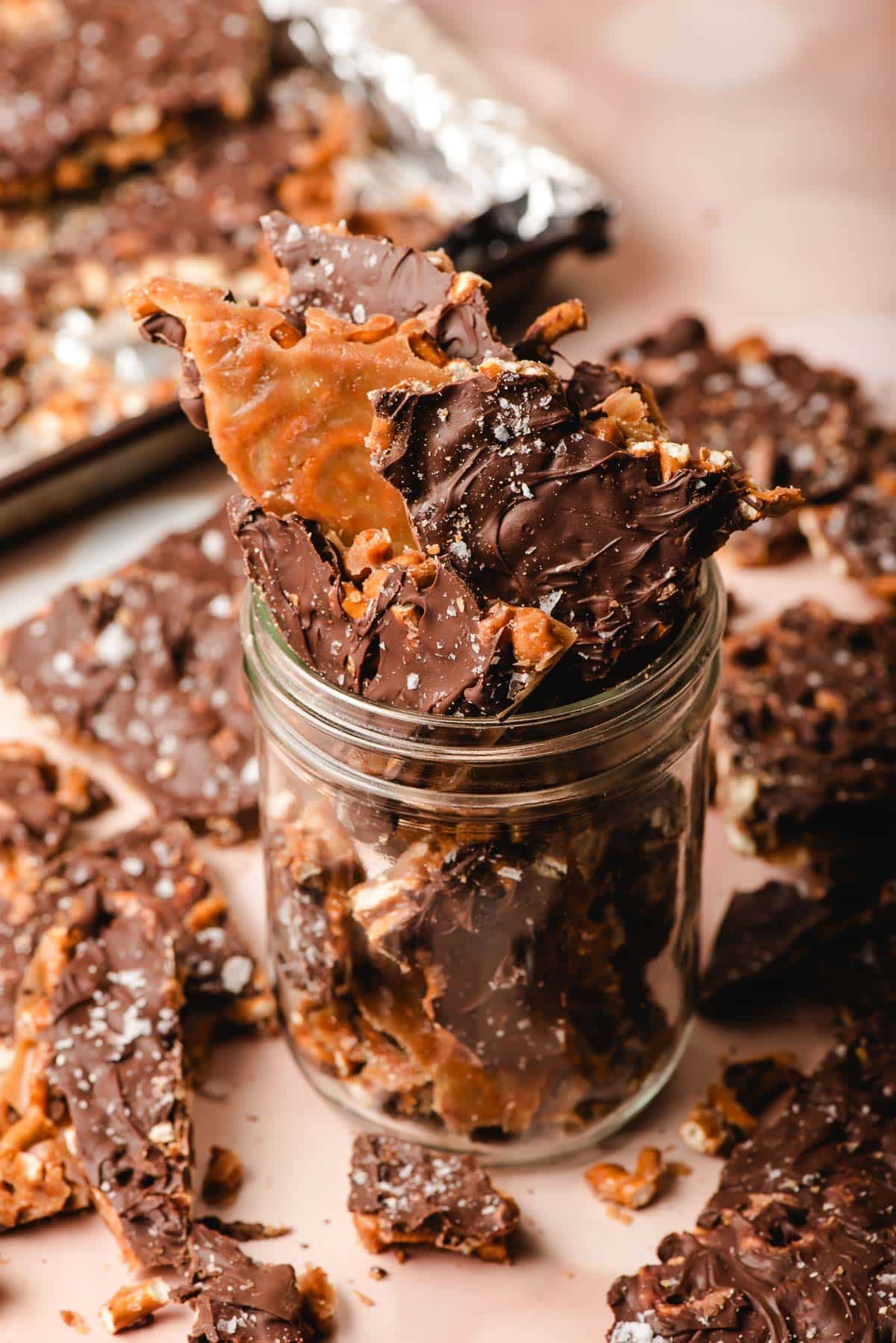 A jar of chocolate pretzel bark on a table with pieces.