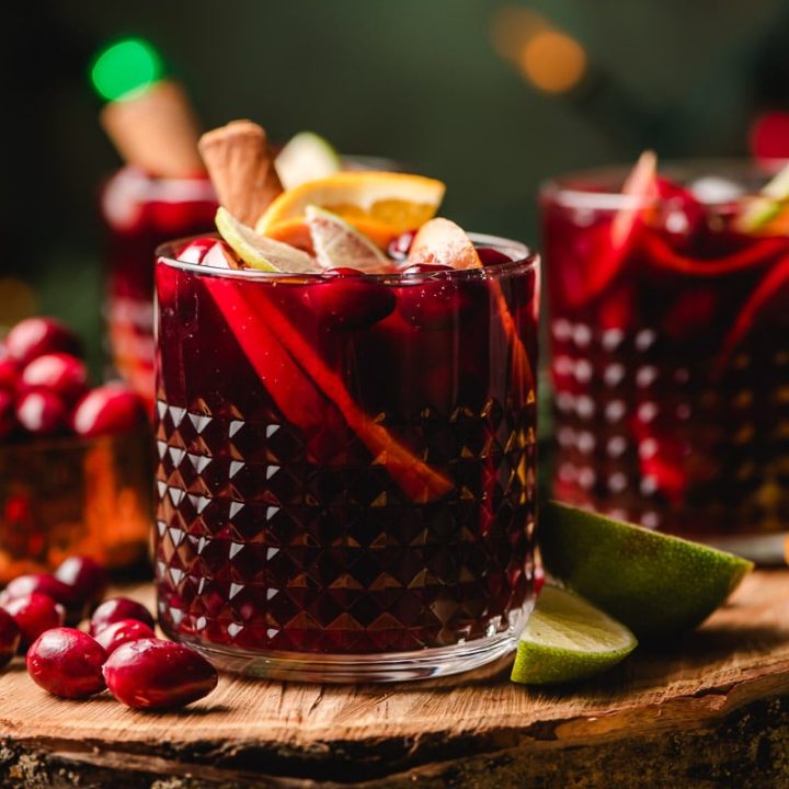 Christmas sangria with apples, oranges, and limes in pretty glasses on a wood serving board.