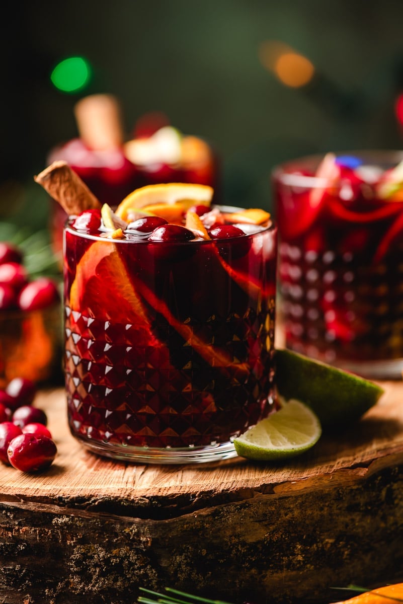 Glasses of Christmas sangria with apples, oranges, limes, and a cinnamon stick.
