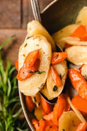 Spoon holding roasted parsnip and carrot slices topped with honey and thyme.