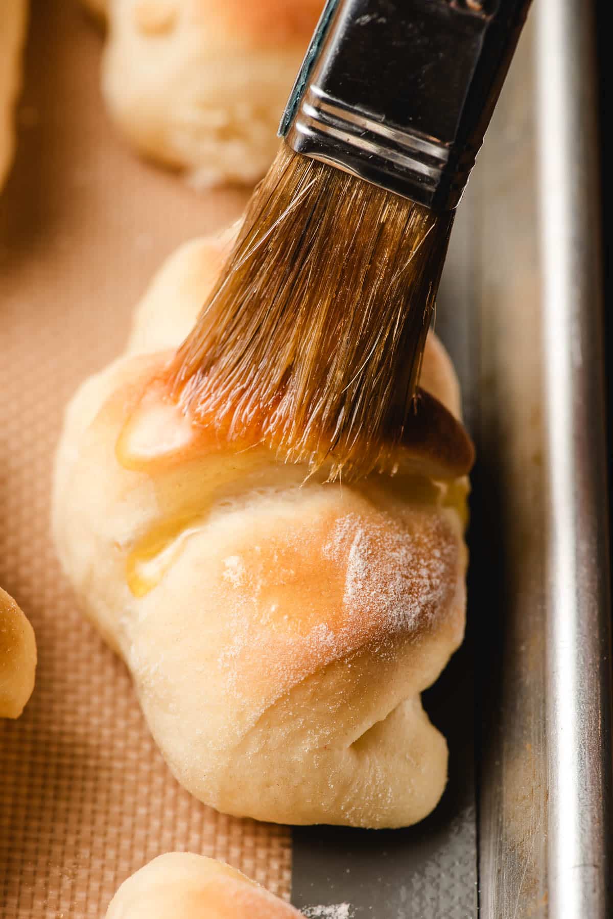 Brushing melted butter onto a warm butterhorn dinner roll.