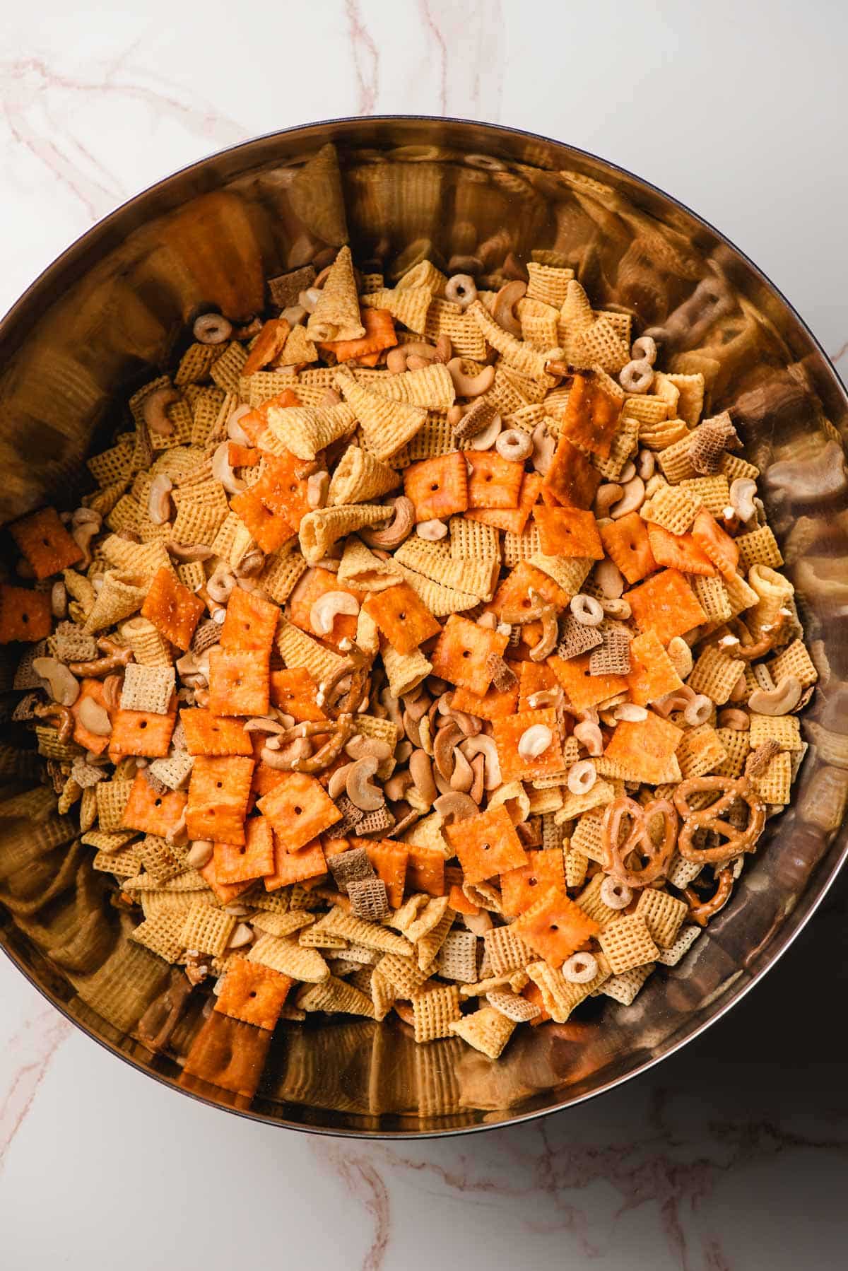 A large mixing bowl full of various snacks for making ranch chex mix.