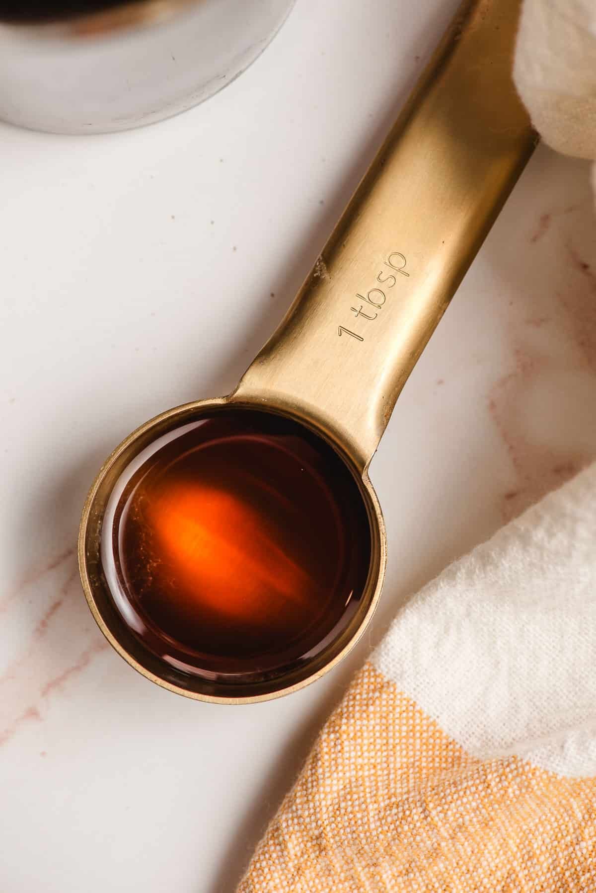 A gold measuring spoon holding cinnamon simple syrup.