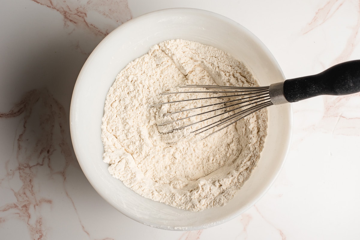 Flour, baking soda, and salt whisked together in a white mixing bowl.